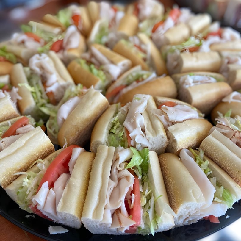 A platter of many turkey and cheese sub sandwiches with lettuce and tomato.