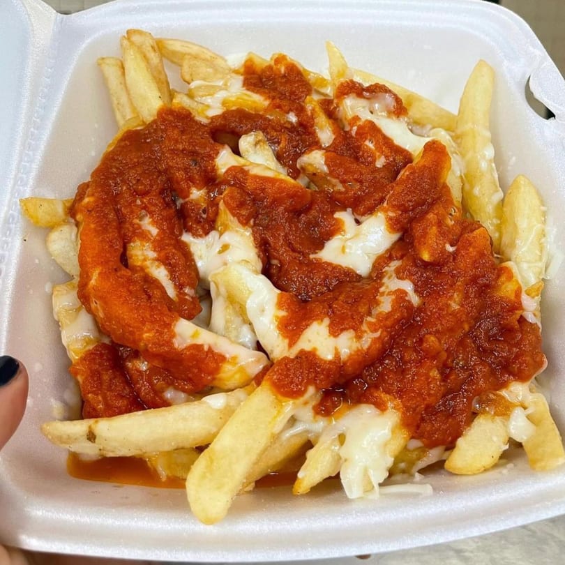 Golden french fries topped with melted cheese and a rich red sauce, served in a white takeout container.
