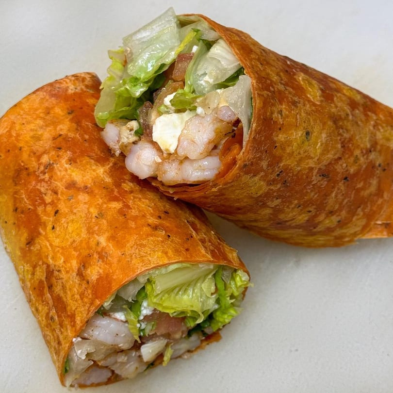 Two halves of a shrimp wrap, filled with lettuce, cheese, and shrimp, on a white surface.
