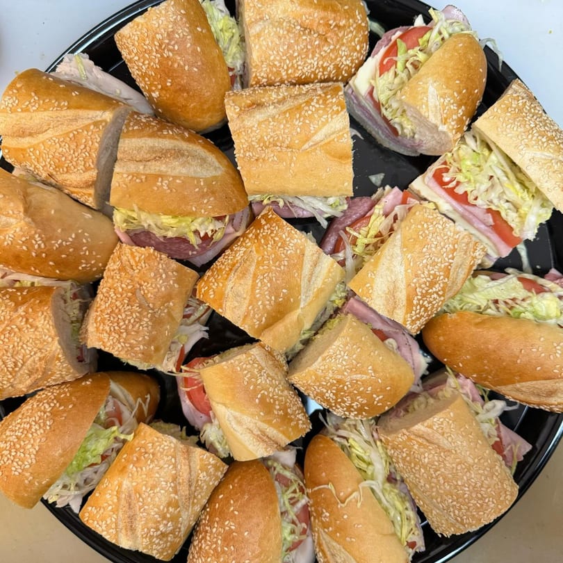 A catering tray filled with many sliced submarine sandwiches on sesame seed rolls with various fillings.