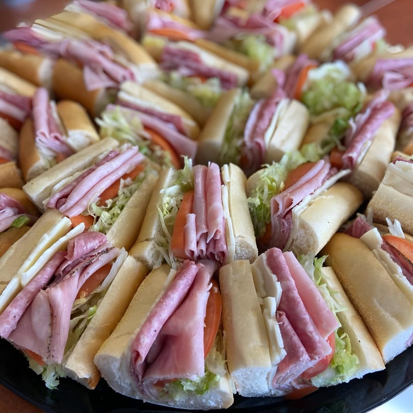 A platter of Sandwich Club's submarine sandwiches, filled with deli meats, cheese, lettuce, and tomatoes.